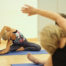 Woman sitting on a yoga mat stretching her arms over her head.