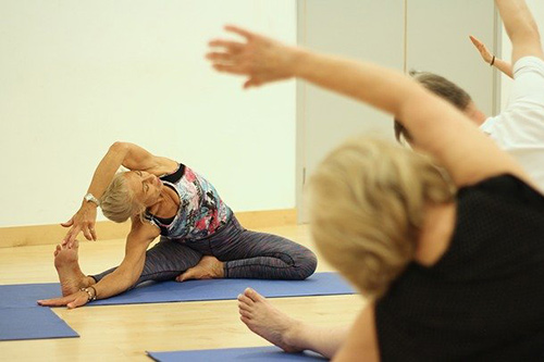 Woman sitting on a yoga mat stretching her arms over her head.