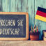Chalkboard that says do you speak german in the german language next to a german flag.