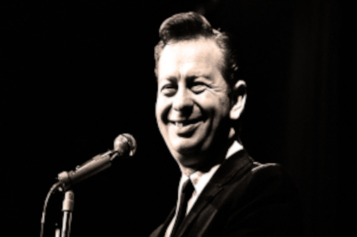 Black and white photo of a smiling Mel Torme next to a microphone