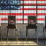 photo of 4 election boxes with flags on them that say vote set against an american flag in the background.